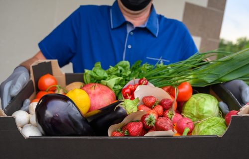 Delivery man in mask holding fresh vegetables box. Home delivery during quarantine