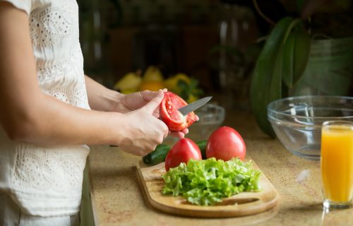 Hands cutting the tomatoes, salad on the board