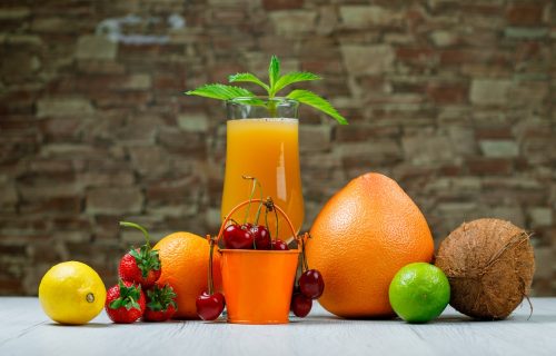 Orange juice with mint, orange, lime, lemon, strawberry, cherry, coconut, grapefruit in a goblet on brick stone and wooden background, side view.